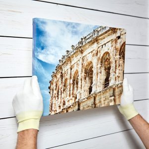 Photography printed on canvas with gallery wrap method of canvas stretching in male hands. Image of architecture of Nimes city, France